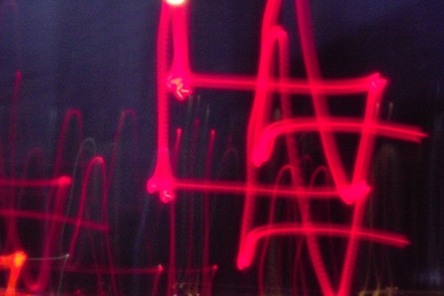 An experimental photograph of looping red light trails against a dark background.