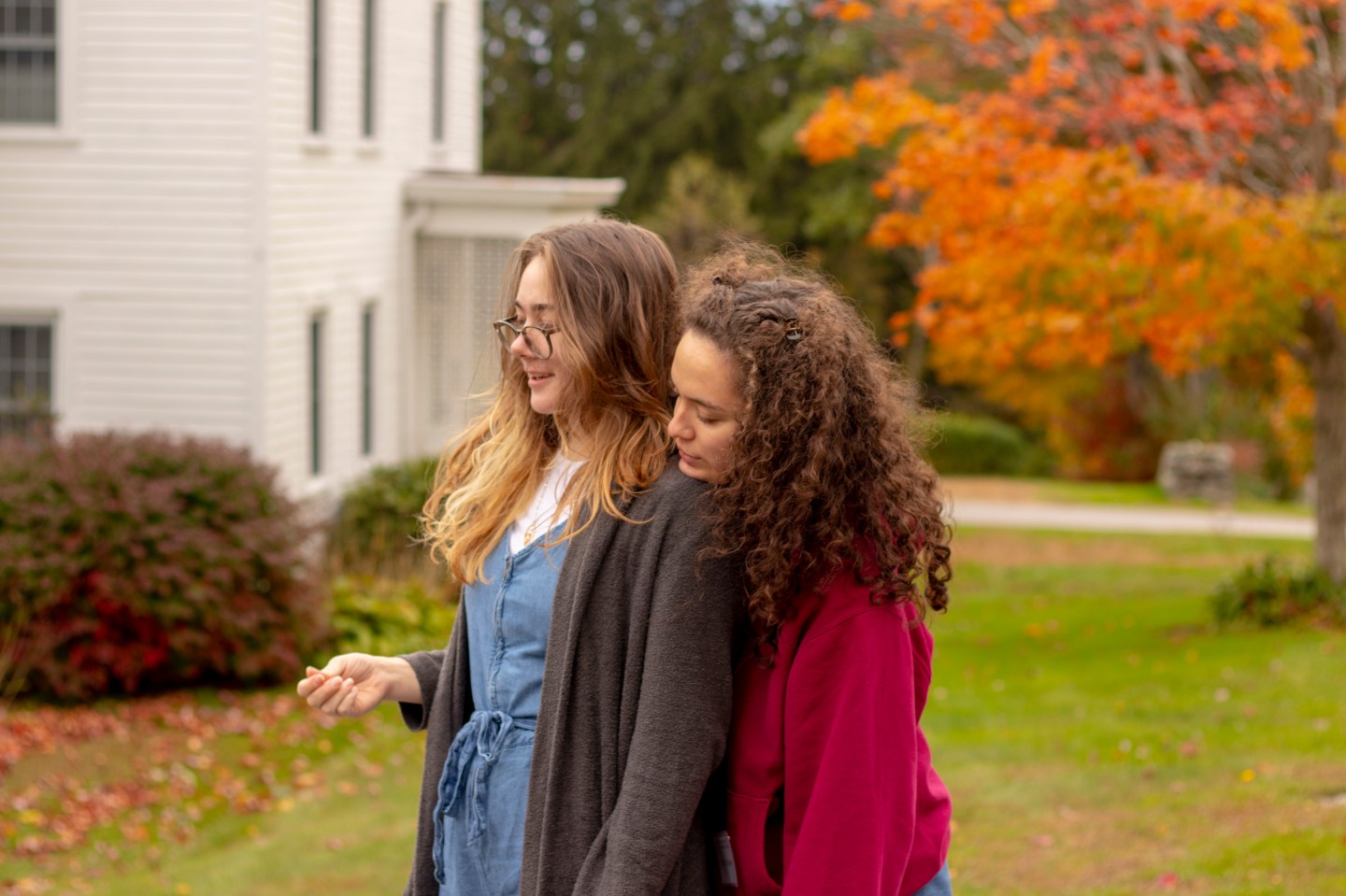 An autumn portrait of two people leaning together outside a white house.